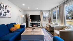A modern living room with a blue sofa, a beige armchair, a wooden coffee table, and a fireplace.