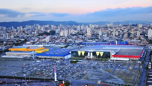 A large parking lot with multiple rows of cars, a prominent yellow building, and a red-roofed structure. - Studio mobiliado Vila Guilherme SP (São Paulo)