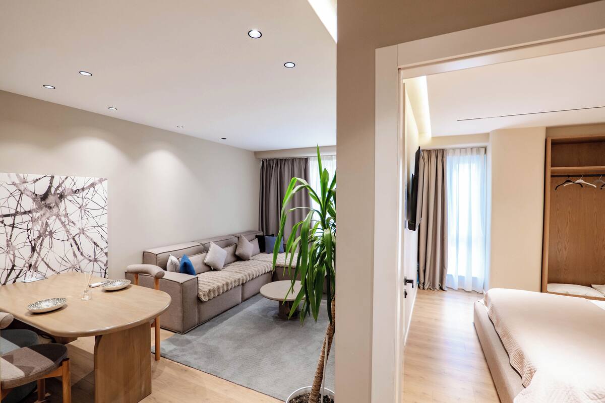 A modern hotel room with a dining area, sofa, and a large plant.