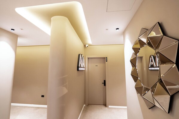 A modern hotel corridor with a geometric wall mirror, a door labeled '203,' and a ceiling with recessed lighting. - Agate Hotel Tirana (Tirana)