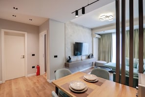 A modern living room with a wooden dining table, a flat-screen TV mounted on the wall, a sofa, and a fire extinguisher. - Agate Hotel Tirana (Tirana)