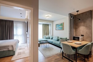 Moderni hotellihuone, jossa on sänky, sohva, ruokailutila ja mikroaaltouuni.