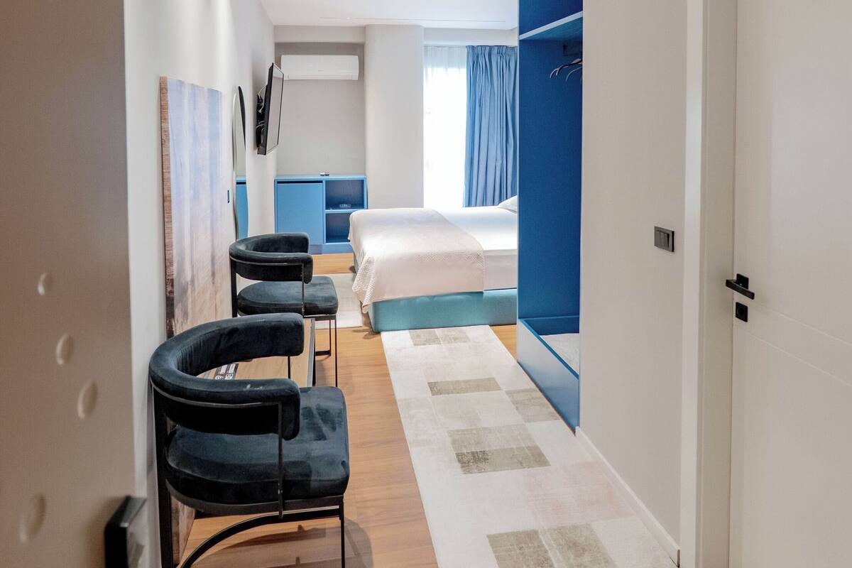 A hotel room with a bed, a desk, a chair, a TV, and a bathroom with a blue door.