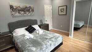 Un dormitorio con una cama, una mesita de noche, un tocador, una puerta y un espejo.