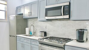 Una cocina moderna con gabinetes grises, un refrigerador de acero inoxidable, un microondas, un tostador, una cafetera y una estufa a gas.