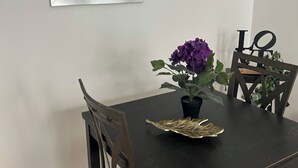 Una mesa de comedor con sillas, un cuadro en la pared y una planta en maceta con flores moradas.