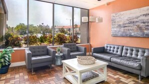 A modern lounge area with grey sofas, a white coffee table, and a large window offering a view of the cityscape. - Wonderful fully furnished 2-bedroom condo in Clearwater Beach. (Clearwater Beach)