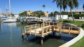 A marina with boats docked, a wooden dock, and a grassy area with palm trees. - Wonderful fully furnished 2-bedroom condo in Clearwater Beach. (Clearwater Beach)