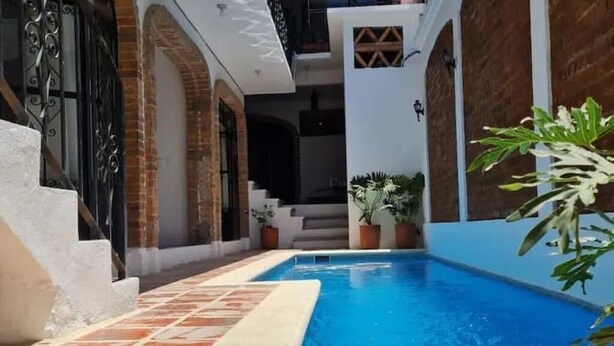 A swimming pool with a tiled deck, surrounded by a building with brick walls and white pillars. - 101 Apartment Luna Vallarta 4P (Puerto Vallarta)