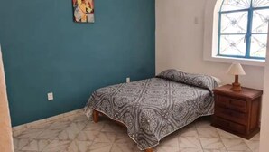 A bedroom with a bed, a nightstand, a window, and a wall with a painting. - 101 Apartment Luna Vallarta 4P (Puerto Vallarta)