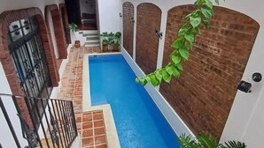 Una piscina estrecha con solárium de azulejos, rodeada de muros de ladrillo y una reja metálica.