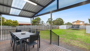 Un patio couvert avec une table et des chaises, un trampoline et une cour arrière clôturée.