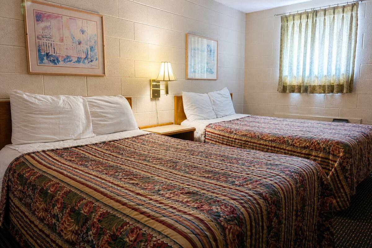 A hotel room with two beds, a nightstand, a lamp, and two framed pictures on the wall.