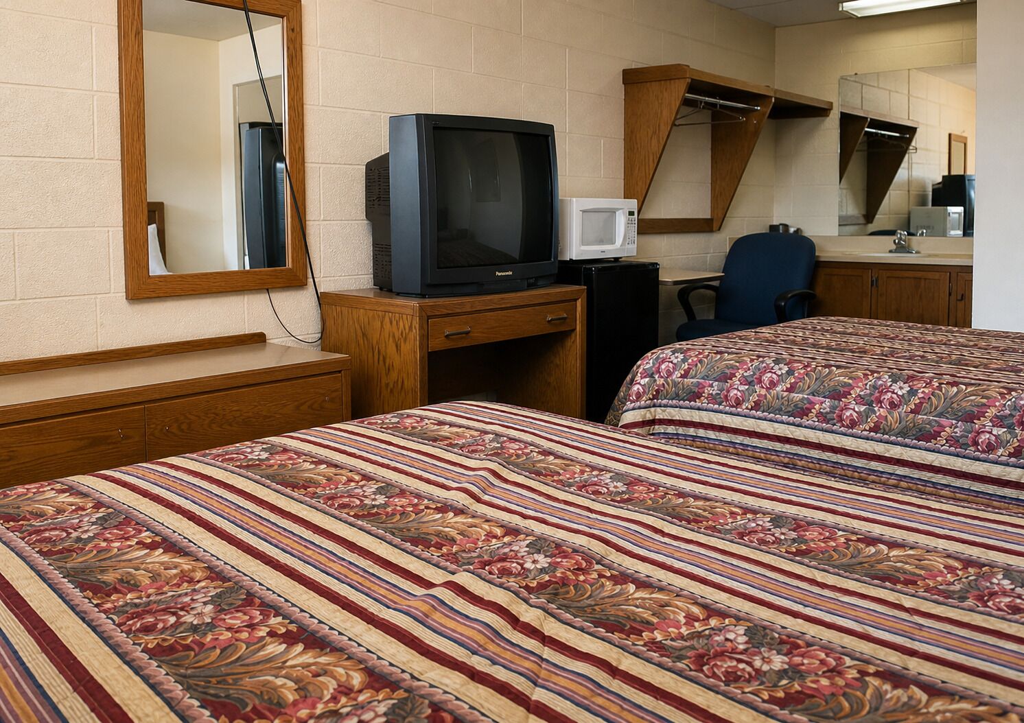 Habitación de hotel con dos camas, televisión, microondas, escritorio y una silla.