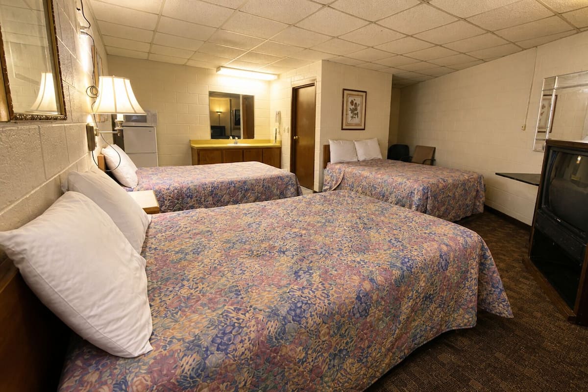 A hotel room with two beds, a desk, a mirror, a television, and a bathroom.