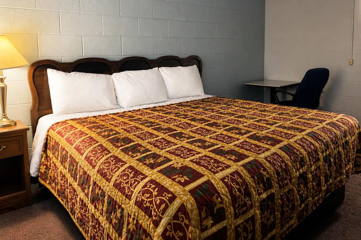 A hotel room with a large bed, a nightstand, a lamp, a chair, and a small table.
