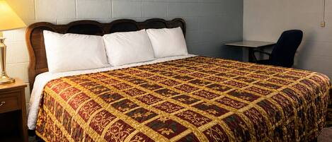 Una habitación de hotel con una cama grande, una mesita de noche, una lámpara, una silla y una pequeña mesa.