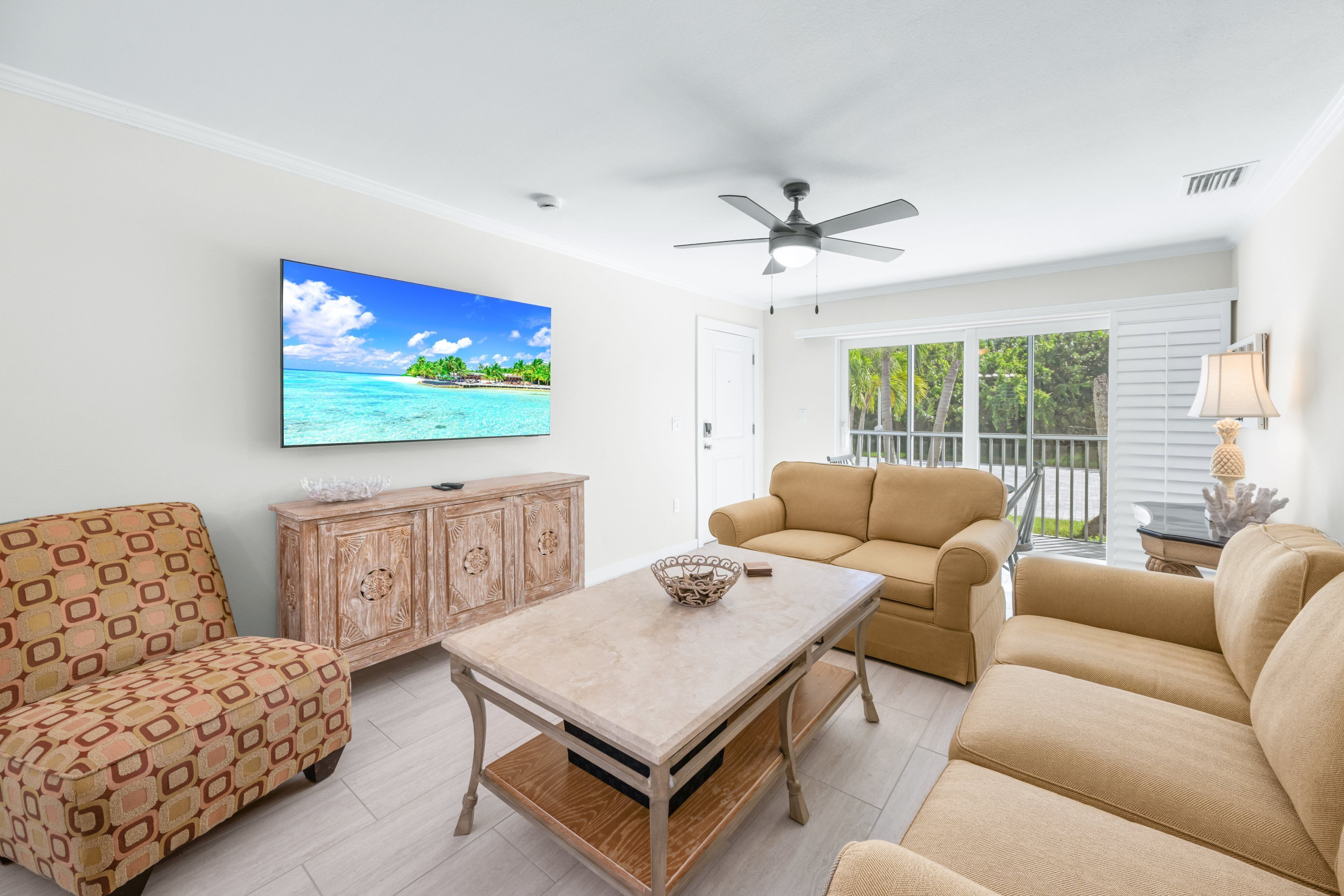 A living room with a TV, a ceiling fan, a wooden cabinet, and a beige sofa.