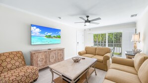 A living room with a TV, a ceiling fan, a wooden cabinet, and a beige sofa.