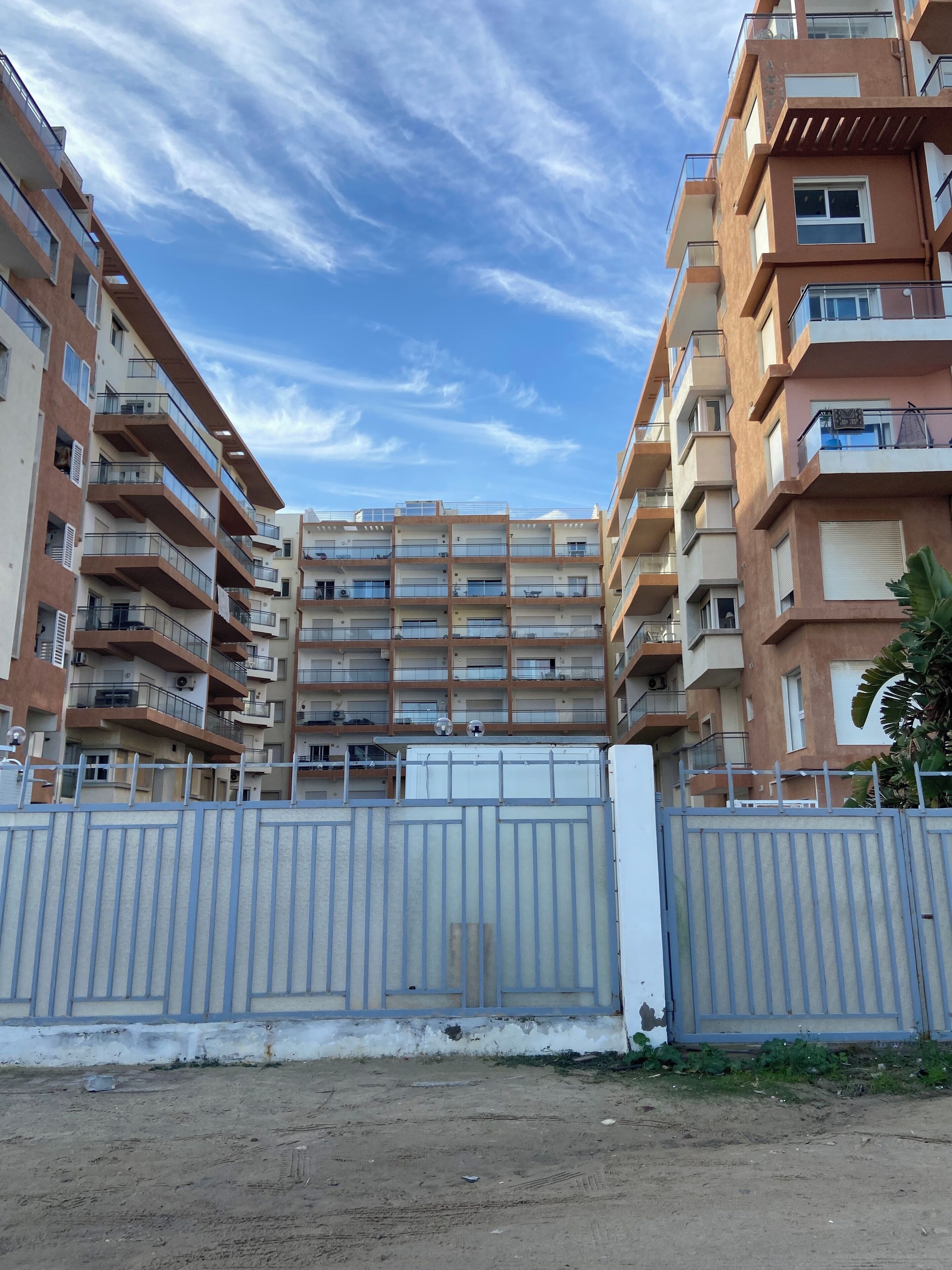Un immeuble résidentiel à plusieurs étages, doté de balcons, d’une entrée sécurisée et surplombant un ciel dégagé.