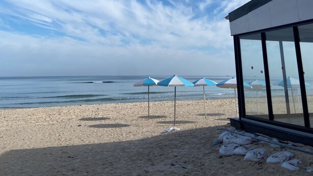 A beach with umbrellas and a building with large windows. - Apartment in secure residence with swimming pool, waterfront location (Sousse)