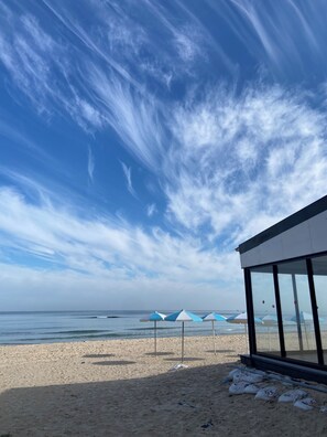 Une plage avec des parasols et un bâtiment doté de grandes fenêtres.