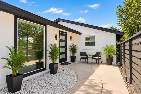 A modern house with a large glass door, a patio with chairs and a table, and potted plants.