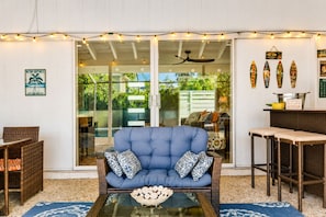 Un espace extérieur accueillant avec un canapé bleu, des fauteuils en osier et une table en verre.