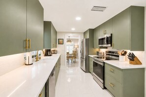 Une cuisine moderne dotée d’un îlot central, d’appareils électroménagers en acier inoxydable et de meubles de rangement verts.