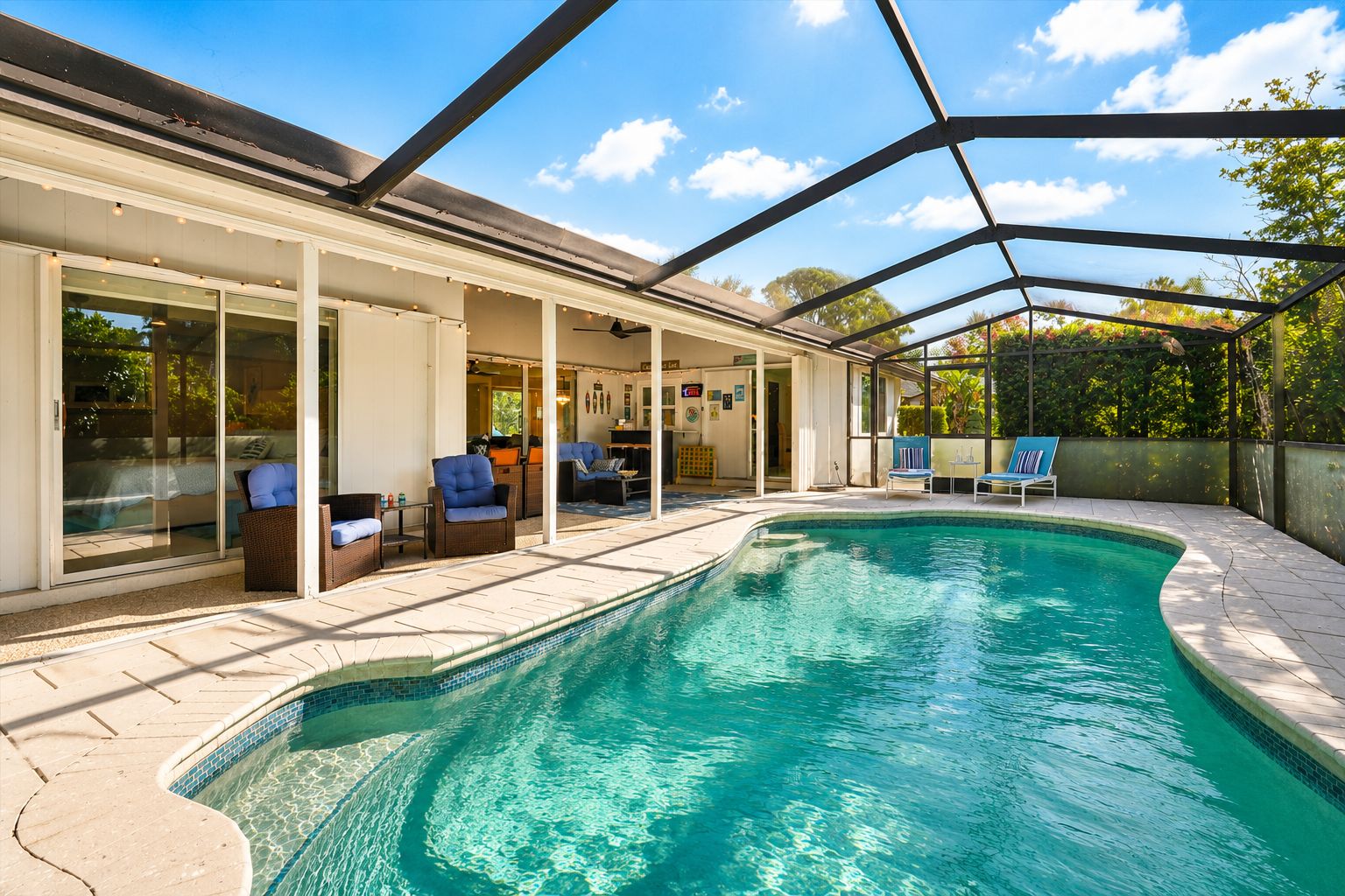 A swimming pool with a covered patio area, lounge chairs, and a view of the sky.