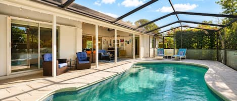 A swimming pool with a covered patio area, lounge chairs, and a view of the sky.