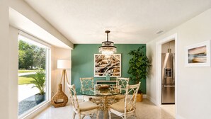 A dining area with a glass table, wicker chairs, a chandelier, a large plant, and a refrigerator. - Private Pool • 10 Min to Siesta Key Beach • Stylish Sarasota Retreat (Sarasota)