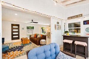 A modern living room with a sofa, a coffee table, and a patterned rug. There is a bar area with stools and a sign that reads 'Live. Love. Eat.'