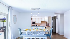 A dining area with a table set for six, a kitchen in the background, and a view through a glass door. - Family home with private heated pool and patio, near Anna Maria Island & IMG. (Bradenton)