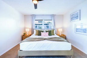A bedroom with a bed, two bedside tables with lamps, a window with curtains, and a ceiling fan.