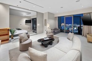 A modern hotel room with a large bed, a sofa, a coffee table, and a TV.