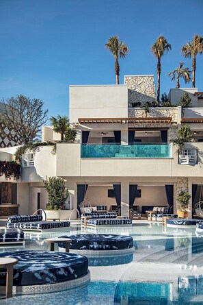 Et moderne hotel med swimmingpool på taget, palmer og en facade af sten.