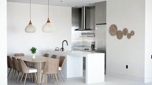Une cuisine moderne dotée d’un îlot central, d’appareils électroménagers en acier inoxydable et de luminaires suspendus.