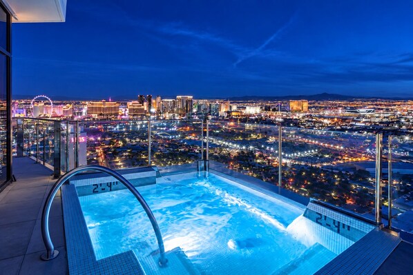A rooftop pool with a cityscape view at night.