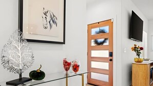 Een modern interieur met een glazen tafel, een witte boomsculptuur en een houten deur.
