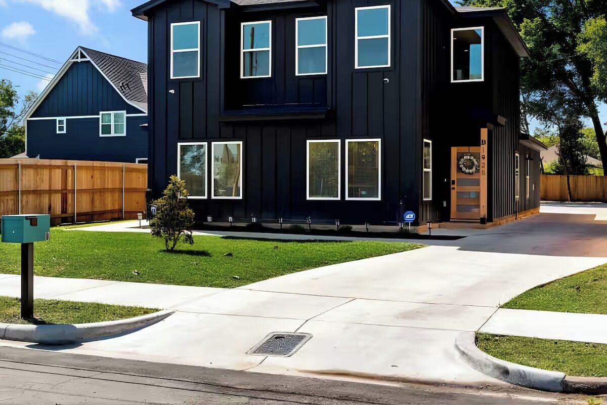 A modern two-story house with a dark exterior, multiple windows, and a well-maintained lawn.