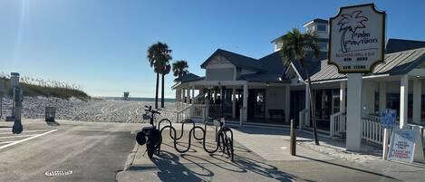 Una propiedad frente a la playa con un letrero que indica Palm Pavilion, un restaurante y bar frente al mar, y un área de estacionamiento designada.