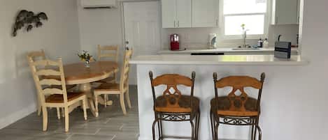 A dining area with a wooden table and chairs, a kitchen with white cabinets, and a window providing natural light.