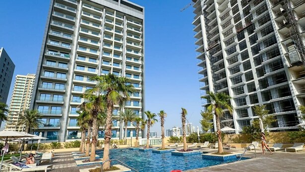 A modern hotel with a rooftop pool surrounded by palm trees and lounge chairs.