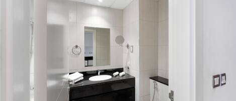 A modern bathroom with a white sink, black countertop, and a glass shower enclosure.