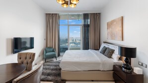 A modern hotel room with a large bed, a TV, a dining area, and a view of the city.
