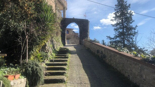 A stone pathway leading to a stone archway, flanked by vegetation and a building with a balcony. - Cà La Torre, Stone House with pool in the terrace and super view (Bibola)