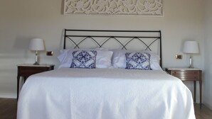 A bedroom with a wooden ceiling, a bed with white bedding, two bedside tables with lamps, and a decorative wall piece above the bed. - Cà La Torre, Stone House with pool in the terrace and super view (Bibola)
