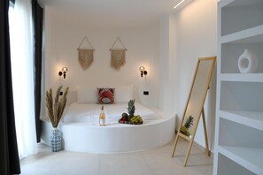 A modern, minimalist room with a curved white sofa, a small table with a bottle and fruit, wall-mounted macramé hangings, and a wooden easel. - Yengeç (Ula)