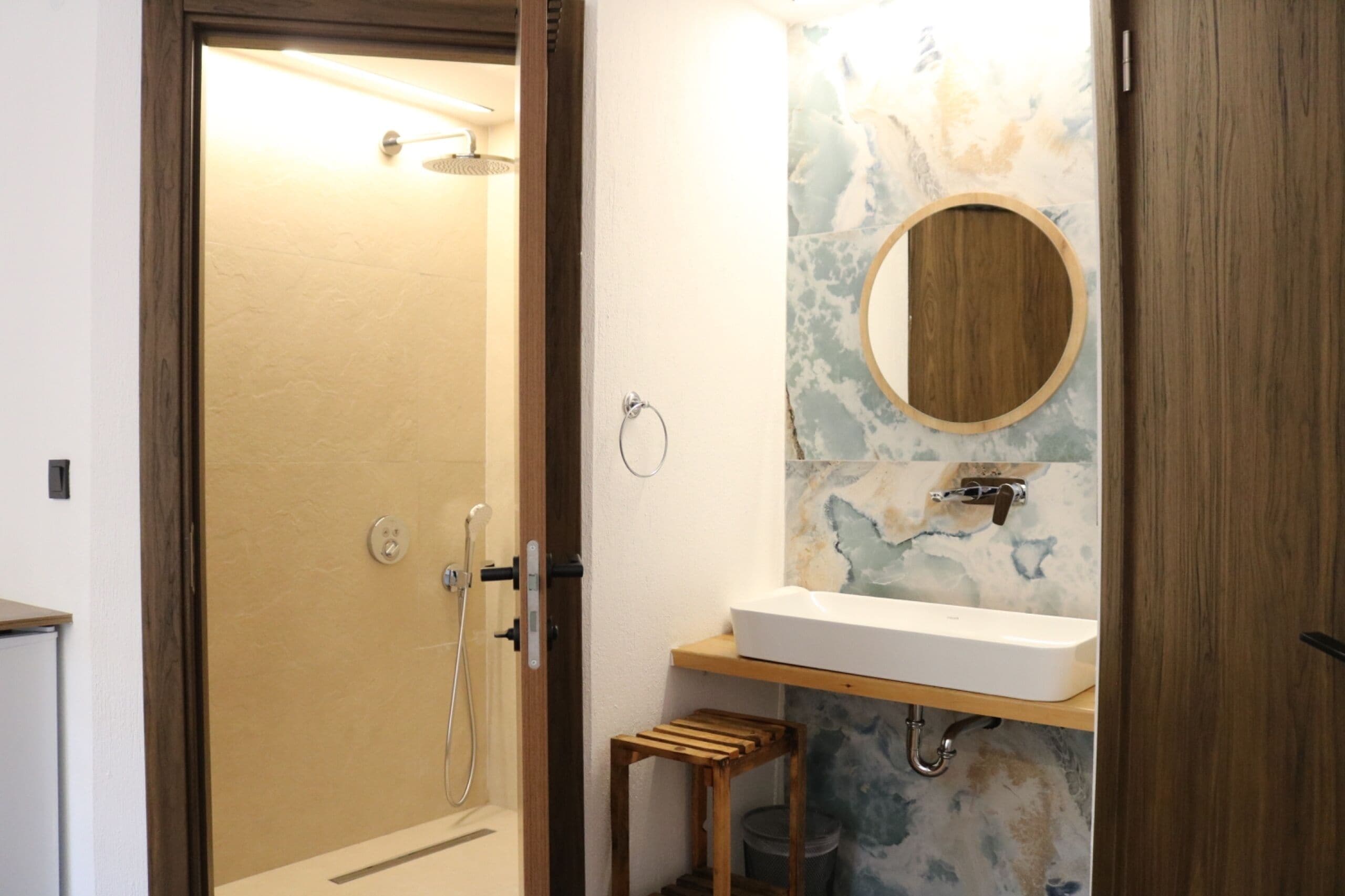 Un baño con ducha, un lavabo, un taburete de madera y un espejo.